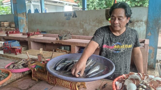 
					Salah satu pedagang memegang ikan yang di jual